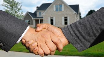 Hand shake with a house in the background.