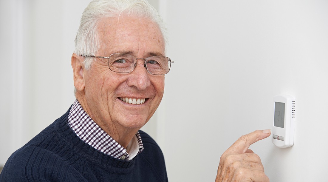 Smiling Senior Man Adjusting Central Heating Thermostat